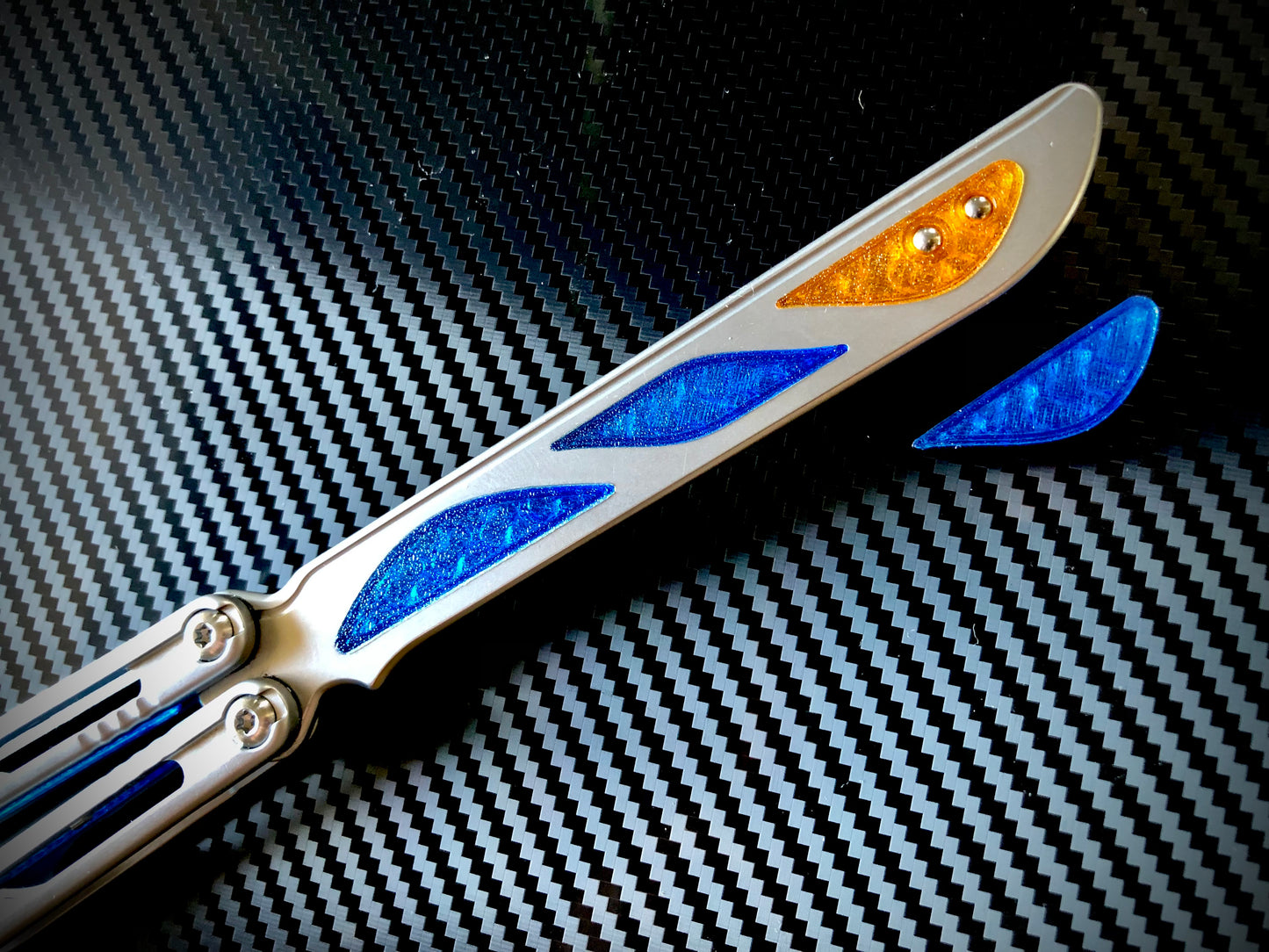 Deepen the sound, silence the ring and adjust the weight distribution of your Nabalis Canyon balisong these custom-made Zippy inlays. This mod consists of (1) speed channel inlays which silence 90% of the ring; as well as optional (2) jimping plugs which silence the ring and house a removable tungsten weight for handle-bias lovers; and (3) optional trainer blade inserts to add tip-weight and a pop of color.